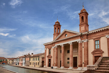 Comacchio, Ferrara, Emilia Romagna, Italy: the ancient hospital Ospedale degli Infermi with church, in neoclassical architecture, at the edge of the canal that crosses the old town - 528090038