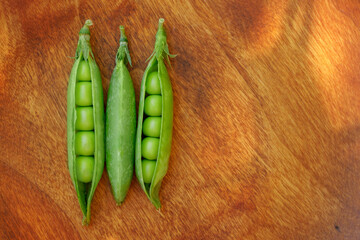 Fresh three green peas on wood texture background. Pea pods are opened.