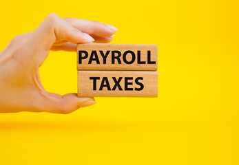 Payroll taxes symbol. Concept word Payroll taxes on wooden blocks. Beautiful yellow background. Businessman hand. Business and Payroll taxes concept. Copy space