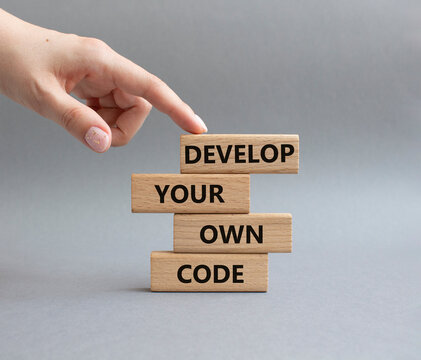 Develop your own code symbol. Concept words Develop your own code on wooden blocks. Businessman hand. Beautiful grey background. Business and Develop your own code concept. Copy space.