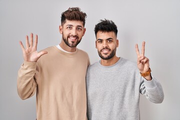 Young homosexual couple standing over white background showing and pointing up with fingers number...