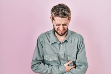 Hispanic man with beard standing over pink background with hand on stomach because nausea, painful disease feeling unwell. ache concept.