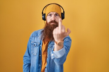 Caucasian man with long beard listening to music using headphones showing middle finger, impolite and rude fuck off expression