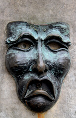 Bronze with verdigris human face, with downturned mouth, set in stone as a water fountain