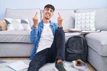 Young hispanic man sitting on the floor studying for university showing middle finger doing fuck...