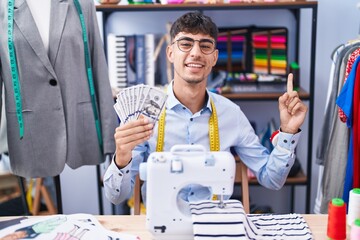 Young hispanic man dressmaker designer holding dollars smiling happy pointing with hand and finger to the side