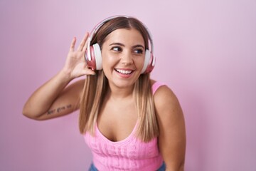 Young blonde woman listening to music using headphones smiling with hand over ear listening an hearing to rumor or gossip. deafness concept.