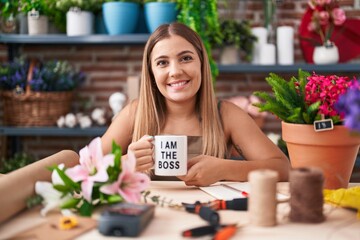 Fototapeta premium Young blonde woman working at florist shop holding i am the boss cup looking positive and happy standing and smiling with a confident smile showing teeth