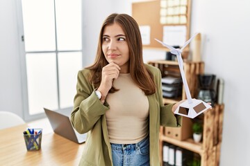 Young brunette woman holding solar windmill for renewable electricity at the office serious face...