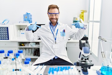 Middle age man working at scientist laboratory looking confident with smile on face, pointing oneself with fingers proud and happy.