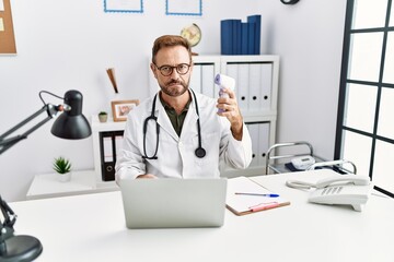 Middle age doctor man holding thermometer at the clinic thinking attitude and sober expression looking self confident