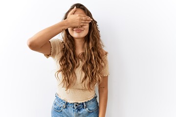 Fototapeta premium Beautiful hispanic woman standing over isolated while background smiling and laughing with hand on face covering eyes for surprise. blind concept.