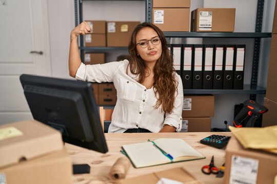 Young hispanic woman working at small business ecommerce strong person showing arm muscle, confident and proud of power
