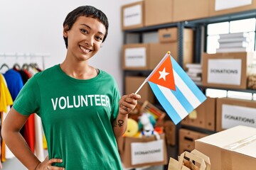 Young hispanic woman wearing volunteer uniform holding cuba flag at charity center