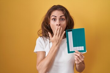 Beautiful brunette woman holding l sign for new driver covering mouth with hand, shocked and afraid...
