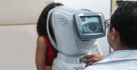 Asian man doctor or optometrist in white coat with eyeglasses using Auto refractometer to examine...