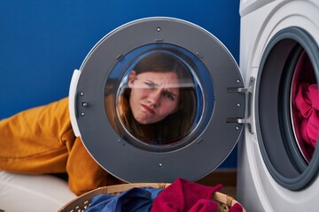 Young brunette woman looking through the washing machine window skeptic and nervous, frowning upset...