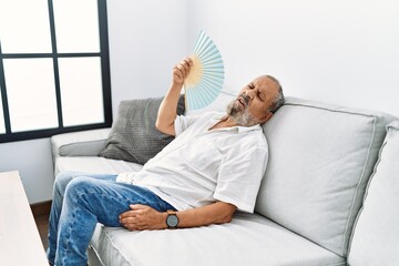 Senior grey-haired man using handfan at home