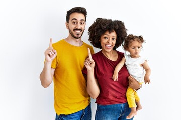 Interracial young family of black mother and hispanic father with daughter pointing finger up with...