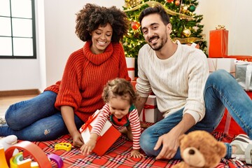 Couple and daughter playing with toys sitting by christmas tree at home