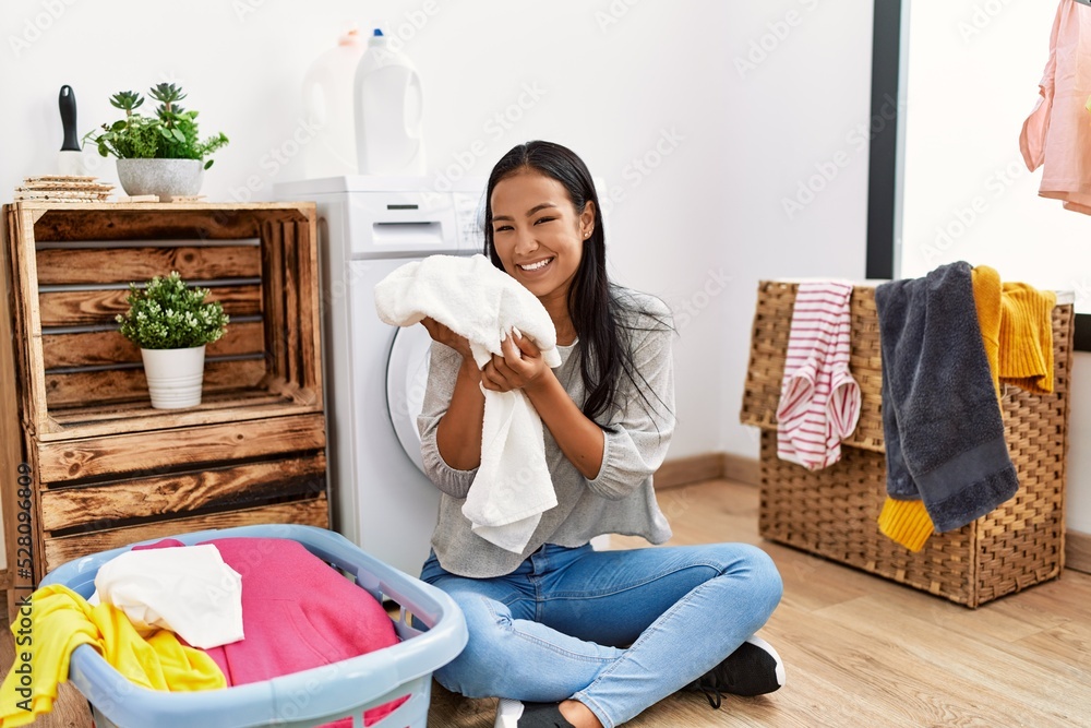 Wall mural Young latin woman smelling clothes at laundry room