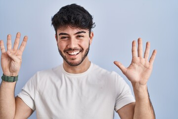 Hispanic man with beard standing over white background showing and pointing up with fingers number...
