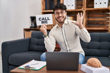 Hispanic man with beard working at therapy office holding call me sign celebrating victory with...