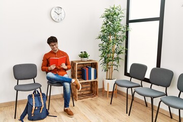 Fototapeta premium Young hispanic man smiling confident reading book at waiting room