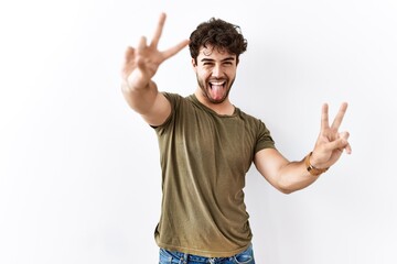 Fototapeta premium Hispanic man standing over isolated white background smiling with tongue out showing fingers of both hands doing victory sign. number two.