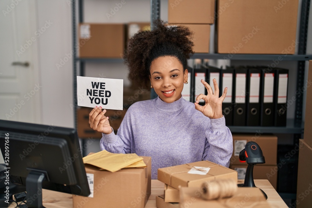 Poster Young african american woman working at small business ecommerce holding banner doing ok sign with fingers, smiling friendly gesturing excellent symbol - Posters