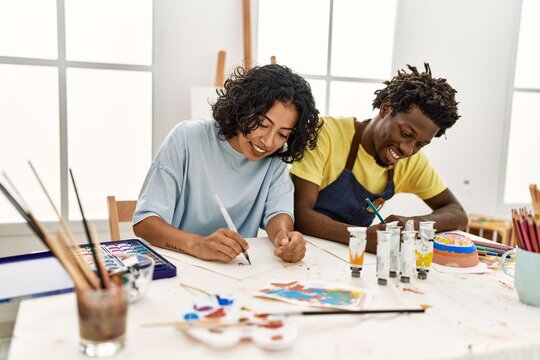 African american artist couple smiling happy painting sitting on the table at art studio.