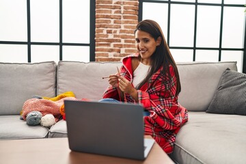 Young hispanic woman sewing using lane and needle watching online lesson at home
