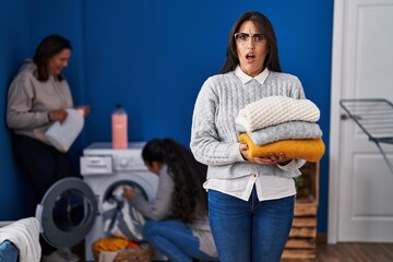 Three women doing laundry at home in shock face, looking skeptical and sarcastic, surprised with open mouth