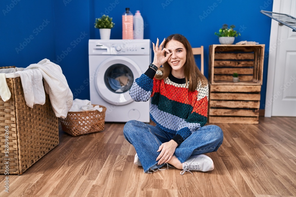 Poster Young hispanic girl doing laundry smiling happy doing ok sign with hand on eye looking through fingers