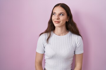 Young hispanic girl standing over pink background smiling looking to the side and staring away thinking.