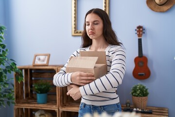 Young hispanic girl opening cardboard box depressed and worry for distress, crying angry and...