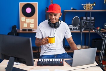 Young latin man musician having dj session drinking coffee at music studio