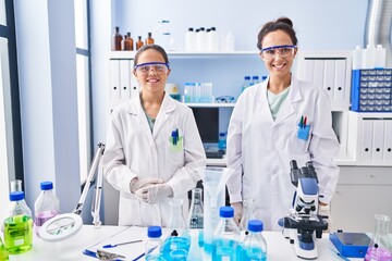 Young mother and daughter at scientist laboratory looking positive and happy standing and smiling with a confident smile showing teeth