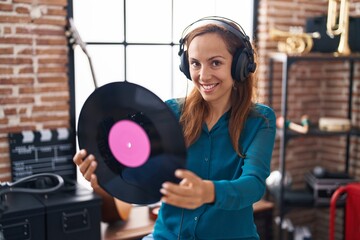 Young woman artist listening to music holding vinyl disc at music studio
