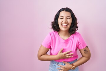 Young hispanic woman standing over pink background smiling and laughing hard out loud because funny crazy joke with hands on body.