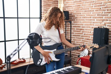 Young beautiful hispanic woman musician smiling confident playing electrical guitar at music studio