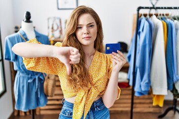 Young caucasian woman at retail shop holding credit card with angry face, negative sign showing...