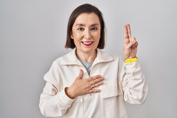 Middle age hispanic woman standing over isolated background smiling swearing with hand on chest and...