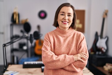 Middle age woman musician smiling confident standing with arms crossed gesture at music studio