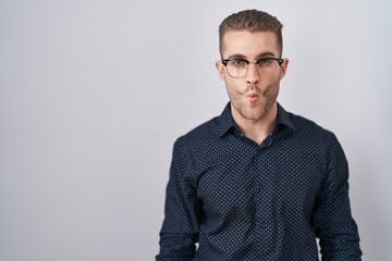 Young caucasian man standing over isolated background making fish face with lips, crazy and comical gesture. funny expression.