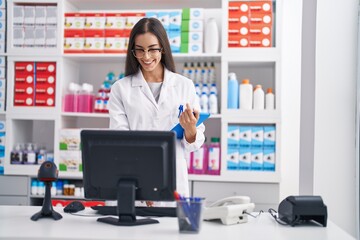 Young beautiful hispanic woman pharmacist using touchpad and computer at pharmacy
