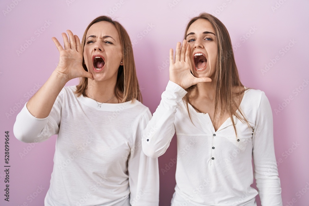 Sticker middle age mother and young daughter standing over pink background shouting and screaming loud to si