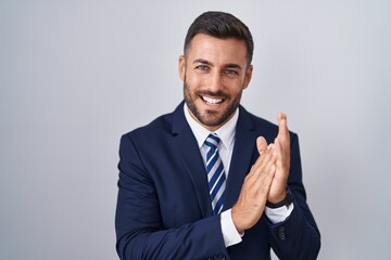 Handsome hispanic man wearing suit and tie clapping and applauding happy and joyful, smiling proud...