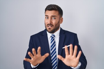 Handsome hispanic man wearing suit and tie afraid and terrified with fear expression stop gesture...