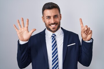 Handsome hispanic man wearing suit and tie showing and pointing up with fingers number six while smiling confident and happy.